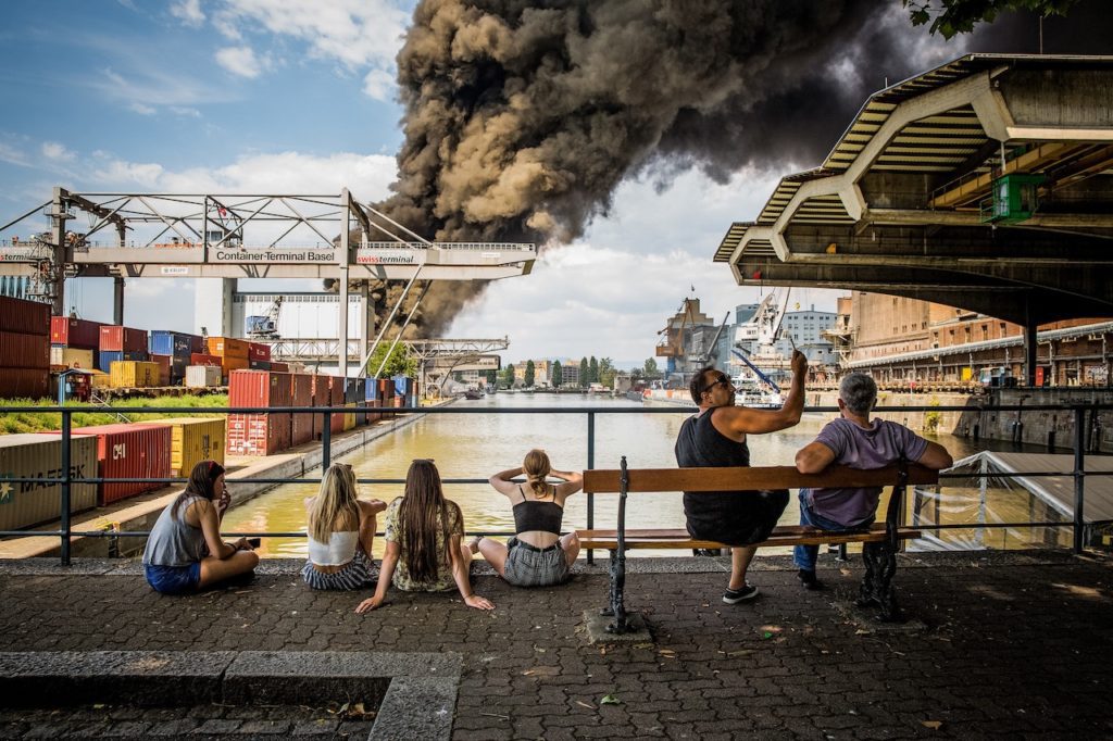 27 мая 2018 года горит старый железнодорожные причал на Рейне в Базеле. Зевак привлекает столб дыма, хотя полиция предупредила об угрозе отравлений. (© Swiss Press Photo / Stefan Bohrer)