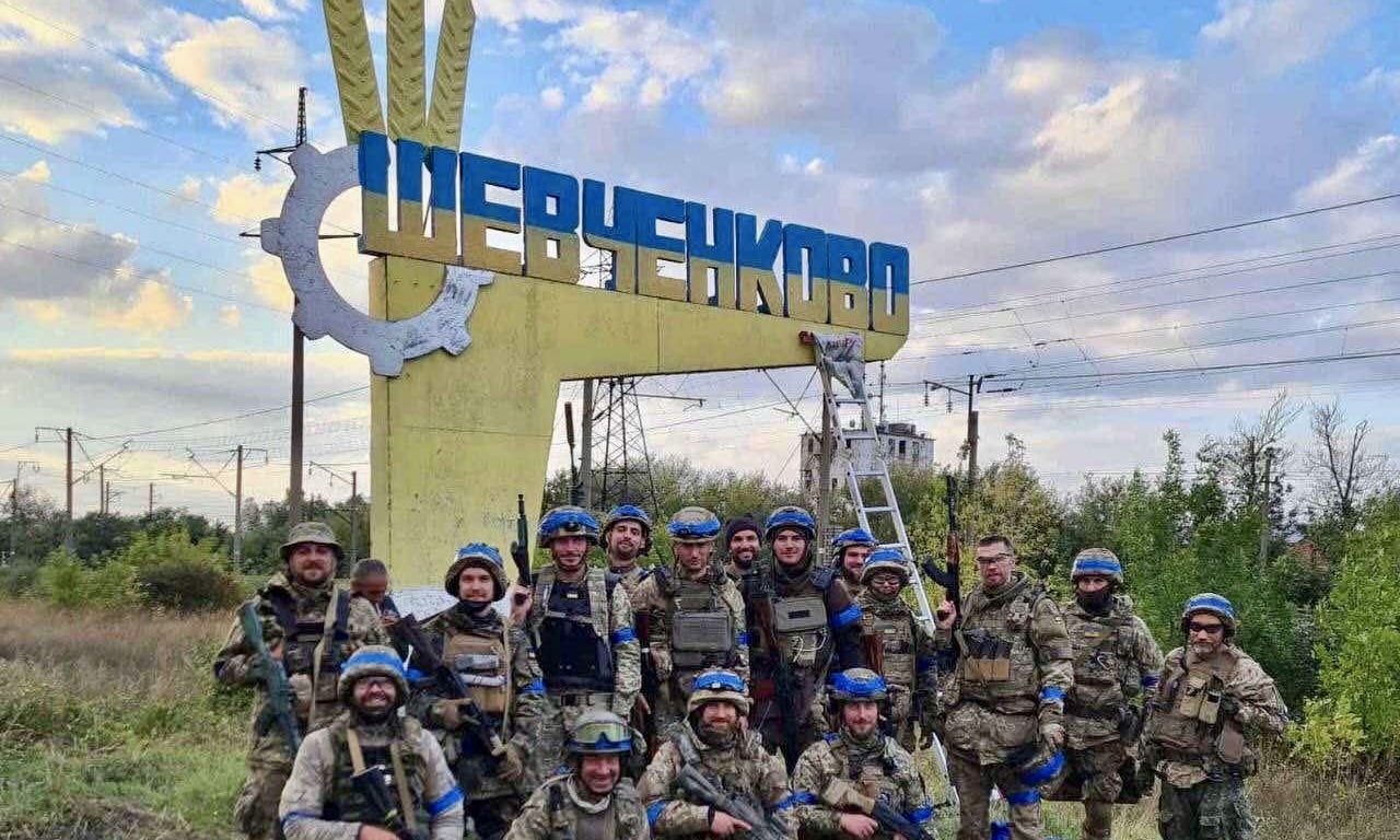 Бойцы теробороны Украины возле свежеперекрашенного (из цветов российского флага на украинский) въездного знака в освобожденном от российской армии поселке Шевченково Харьковской области, 10 сентября 2022 г. (Территориальные силы обороны Украины / mil.gov.ua)